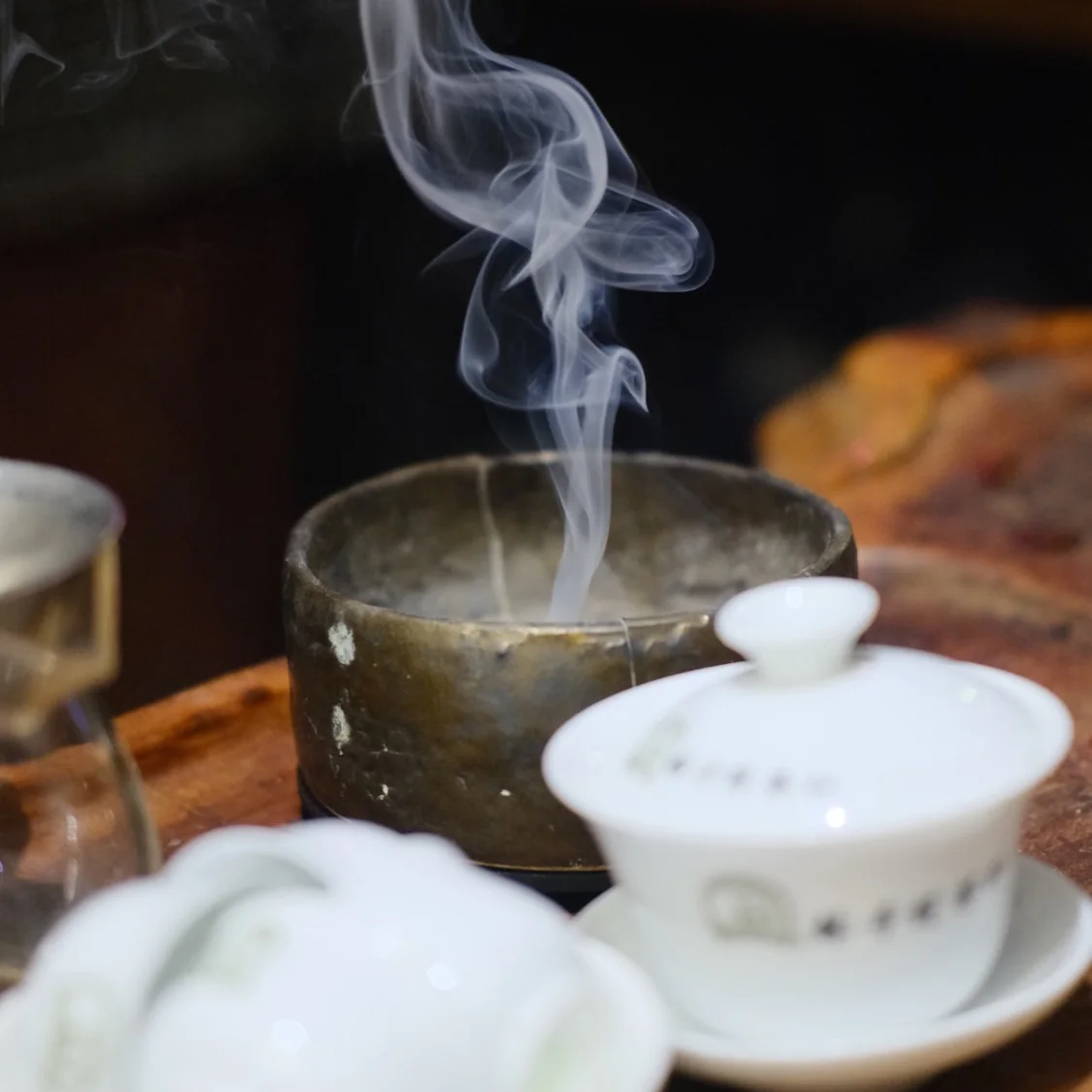 Steam rising over a tea set with a white gaiwan on a wooden tray