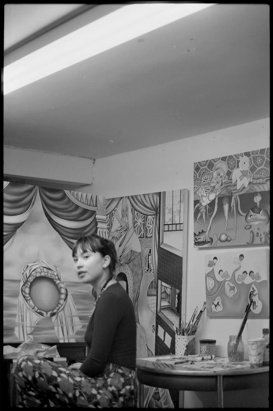 Ashley Yang-Thompson in her studio among paintings, black and white