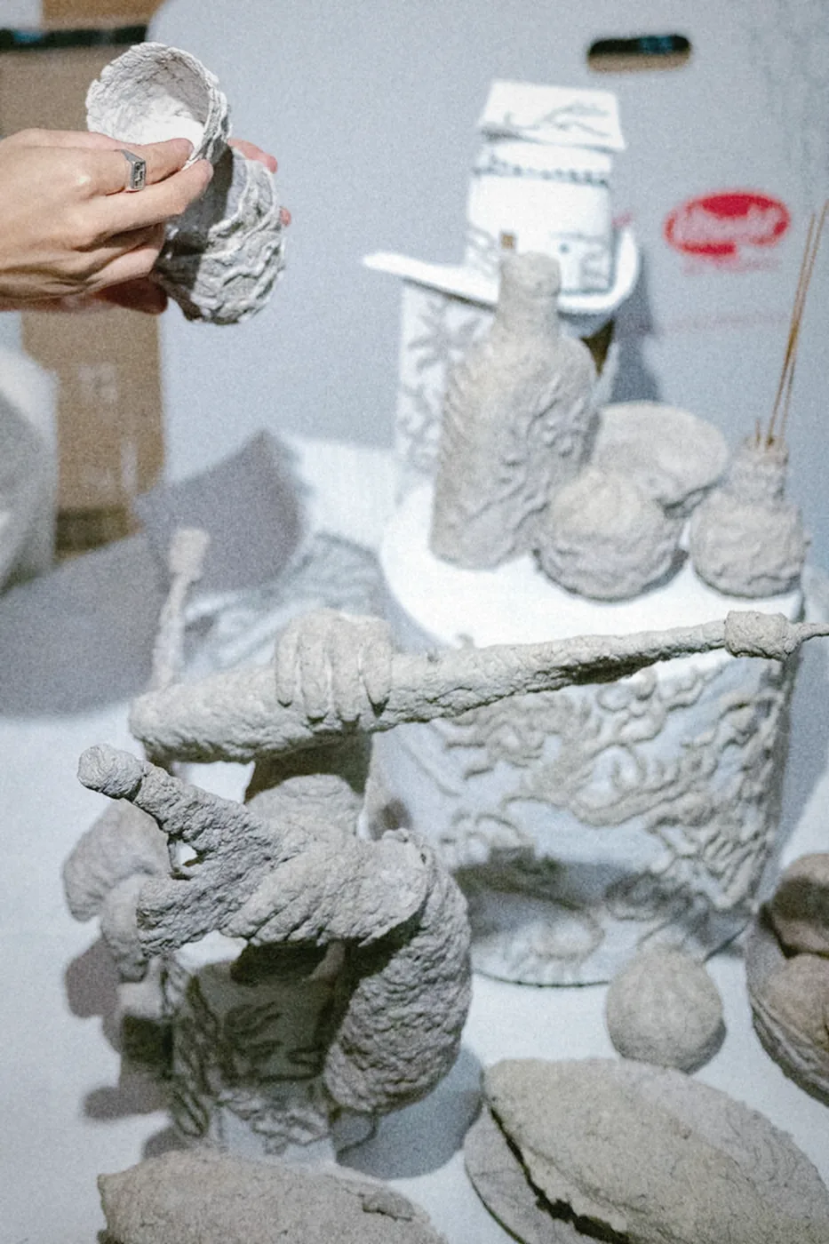 Hands holding a textured grey vessel among studio sculptures