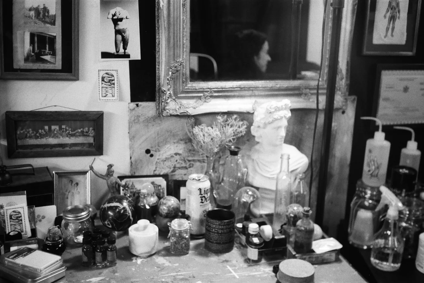 Black-and-white still life of a studio desk with bust and bottles