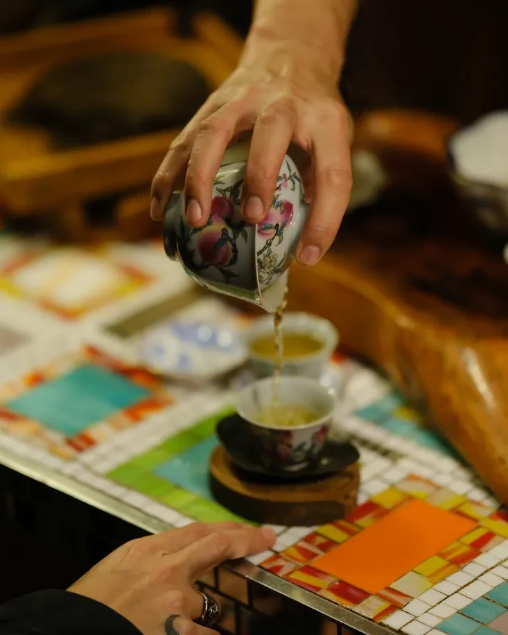 Two hands pouring from a painted gaiwan into waiting cups