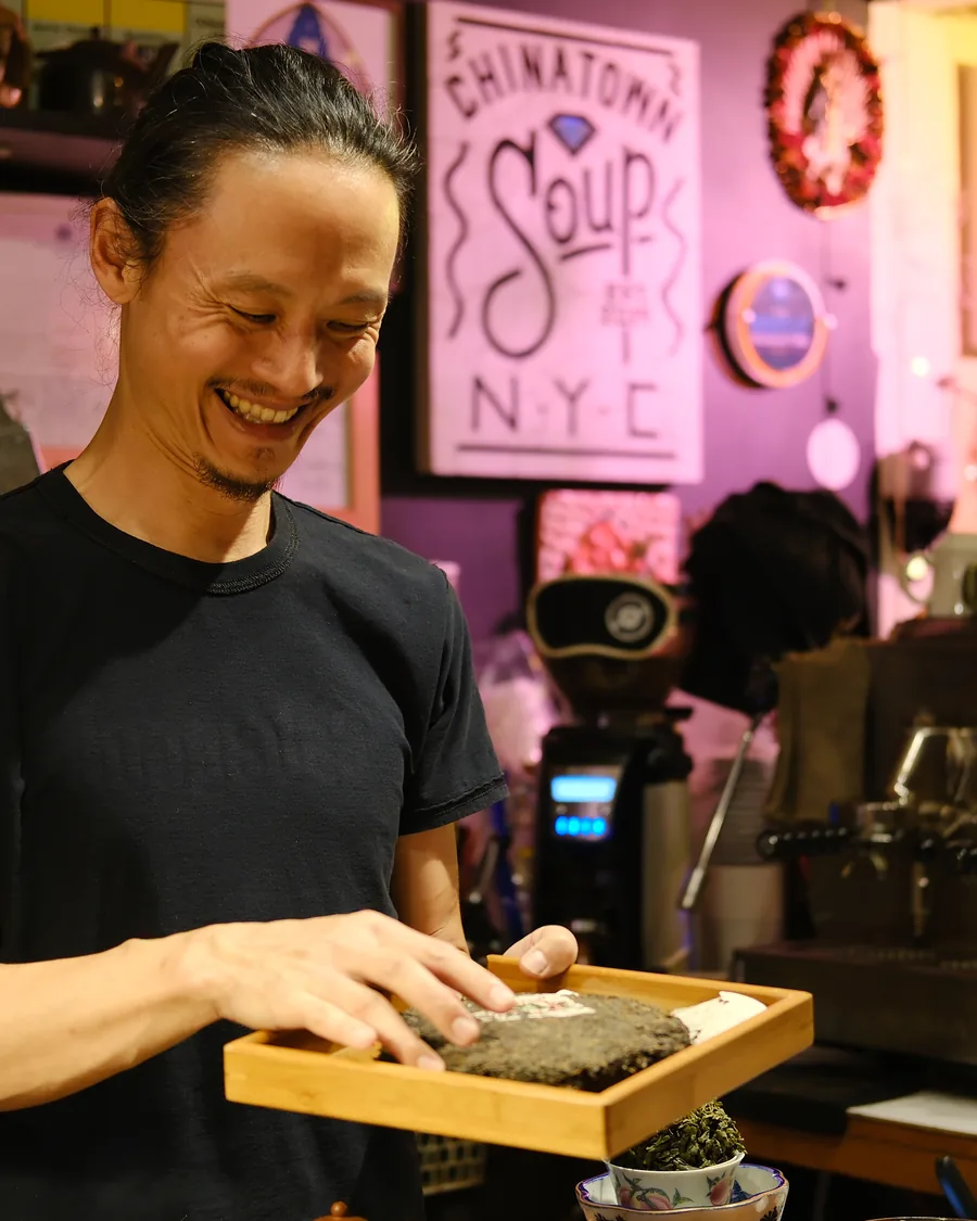 A smiling host carrying a wooden tray of pressed tea past the pink Chinatown Soup wall