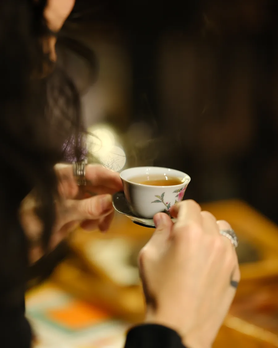 Two hands cradling a small floral cup of steaming tea