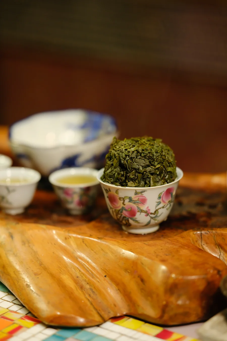 Floral-patterned bowls on a wood-slab table, one heaped with green leaves