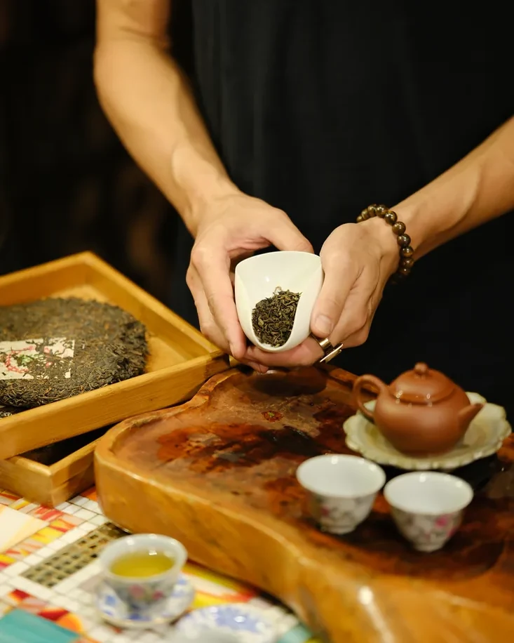 Hands offering a cup of loose leaf tea above the bar, four cups waiting below